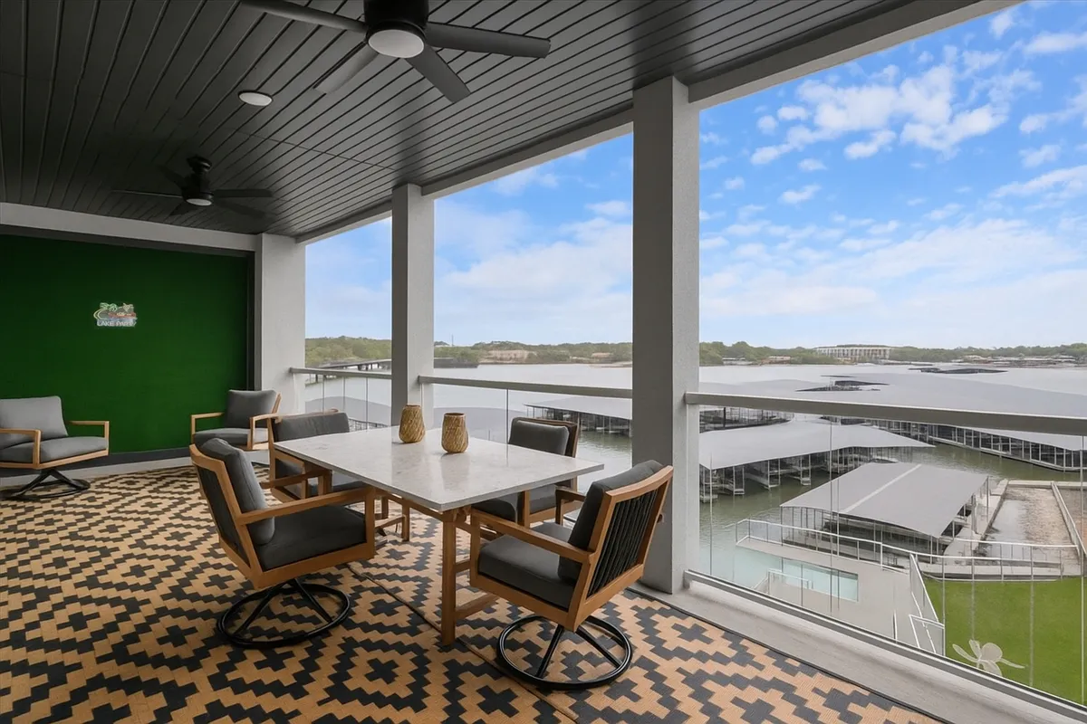 The image showcases a spacious outdoor dining area on a condo balcony overlooking the marina at Lake of the Ozarks. Comfortable chairs surround a modern table on textured flooring, inviting guests to enjoy meals, socialize, and relax while taking in sweeping lake views, watching boats glide by, and soaking up the sunshine.