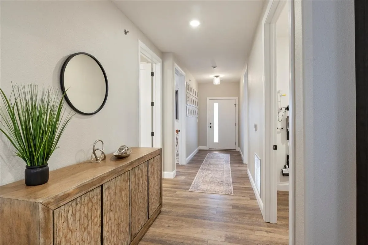 A bright, inviting entryway with a wooden console table, decorative plant, mirror, and front door. The gallery wall and rug create a welcoming ambiance, ideal for first impressions and showcasing secure, accessible entry.