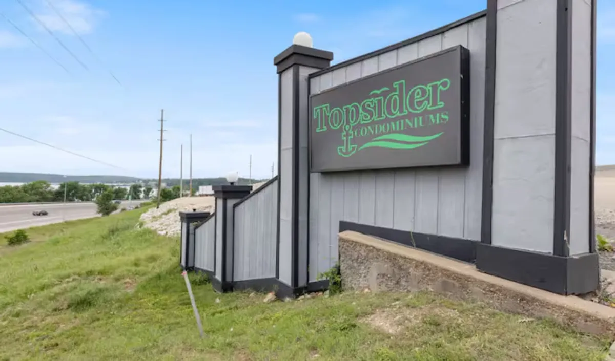 The welcoming entrance to Topsider Condominiums features the property sign, a staircase leading up, and lush greenery surrounding the area. The overall scene suggests a friendly, community-focused environment and serves as a contextual anchor for the property.