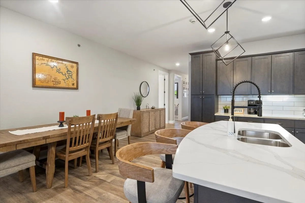 This image focuses on the kitchen island and adjacent dining table, with stylish cabinetry and wall art providing a warm backdrop. The setup signals readiness for casual gathering, family meals, or coffee conversations, and the oversized island allows for group meal prep or serving.