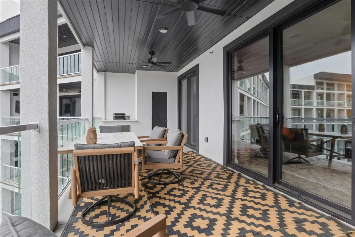 A contemporary outdoor seating area with stylish furniture and decorative flooring, framed by large glass doors that allow natural light to stream in. The scene suggests a tranquil, social spot for morning coffee or sunset conversations.
