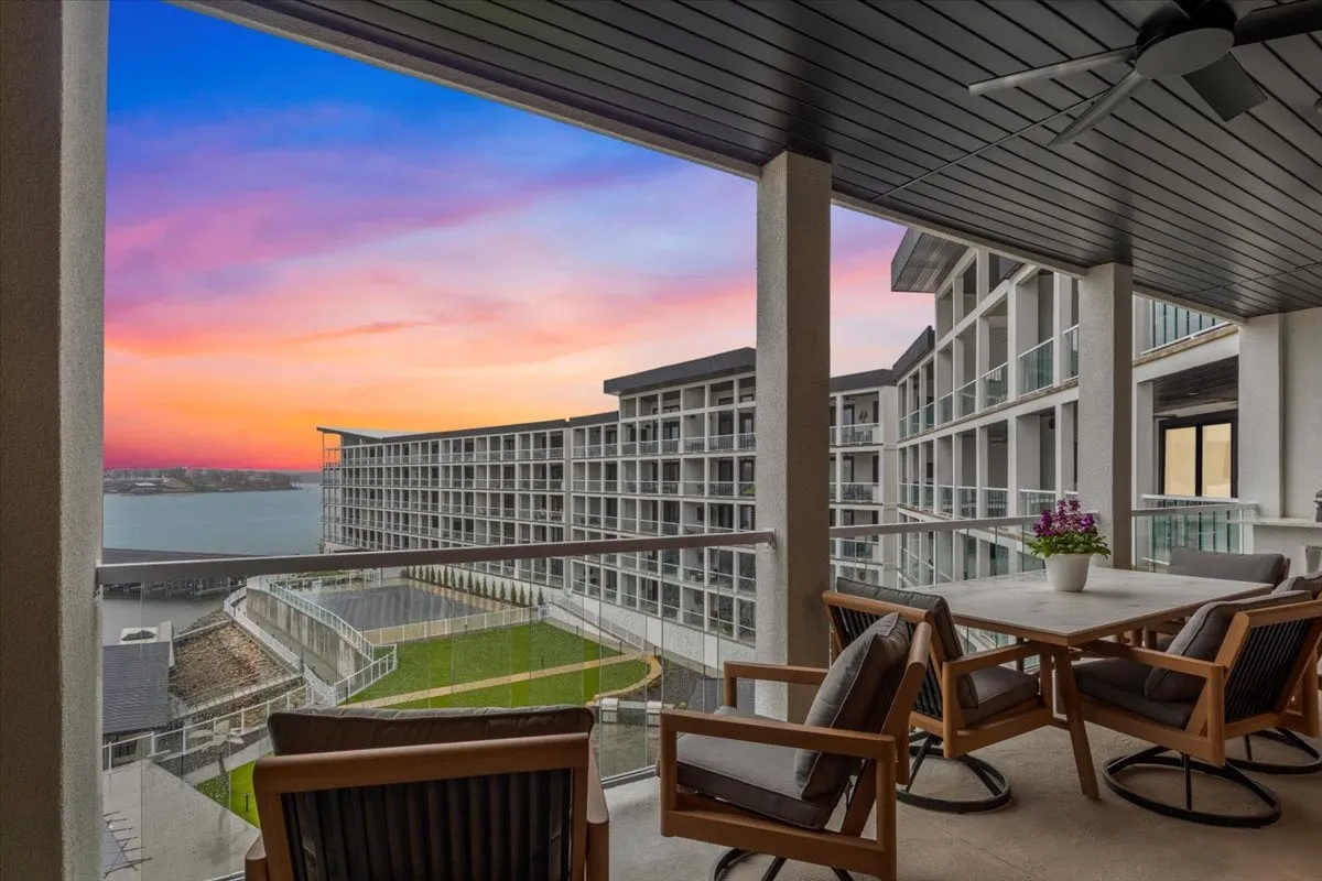 A private balcony with comfortable seating overlooks the main channel of the lake, framed by a breathtaking sunset sky. The scene exudes tranquility and features an alfresco dining setup, creating an inviting space for morning coffee or sunset wine while soaking in the water views.