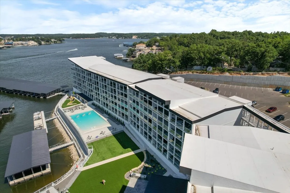 A vibrant exterior scene featuring a sparkling swimming pool, waterfront views, lush green landscaped areas, and the modern architecture of the condominium building. The pool area is lively and inviting, ideal for both relaxation and active fun.