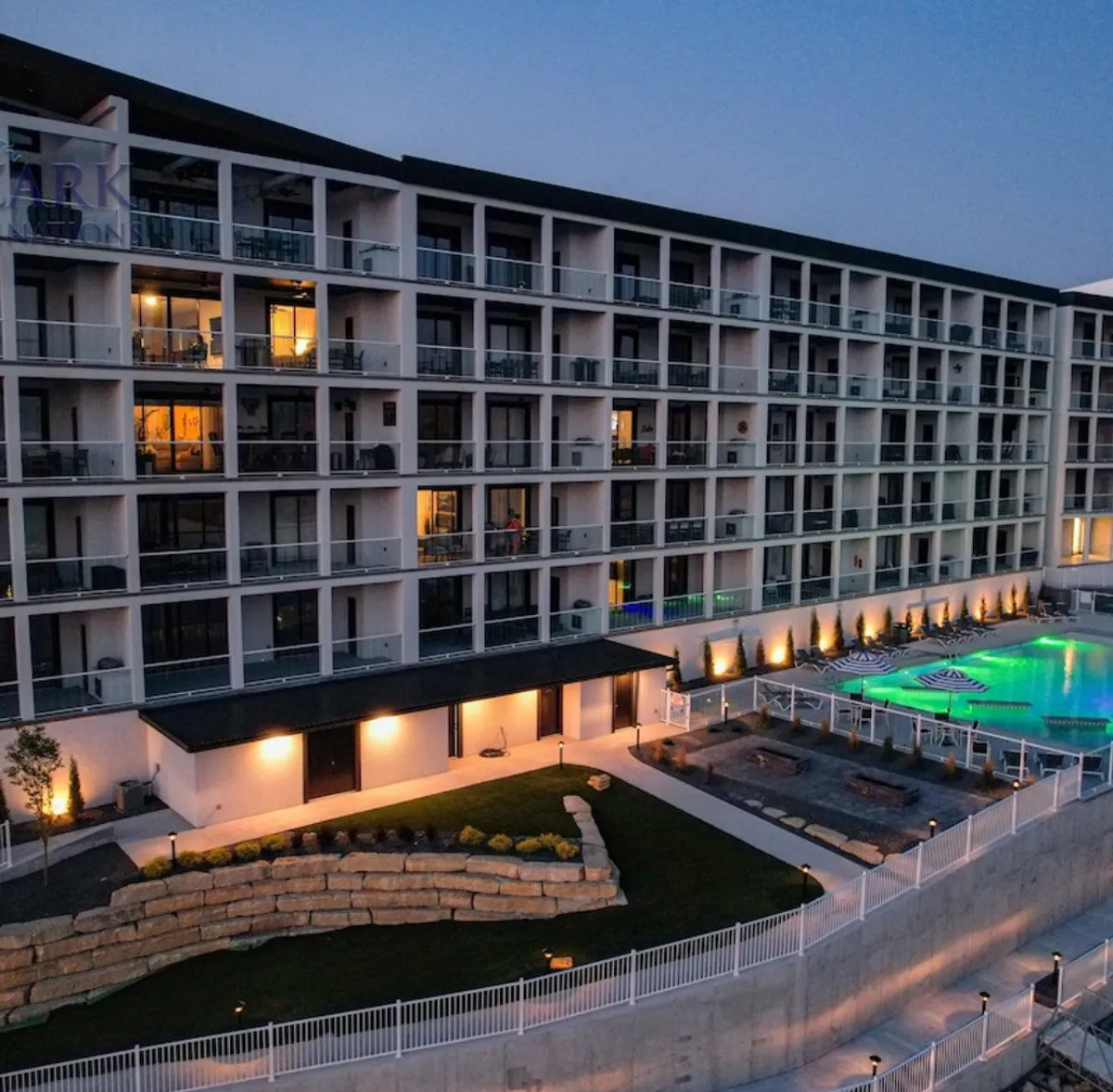 A serene exterior view showcasing a sparkling swimming pool surrounded by lush landscaped gardens and modern balconies. Outdoor seating areas are arranged for relaxation and socializing, with the inviting pool as a central feature.