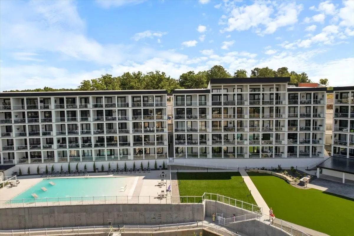 A refreshing scene highlighting a swimming pool area bordered by green lawns and trees, with balconies overlooking the space. The environment feels tranquil and perfect for both relaxation and community gatherings.